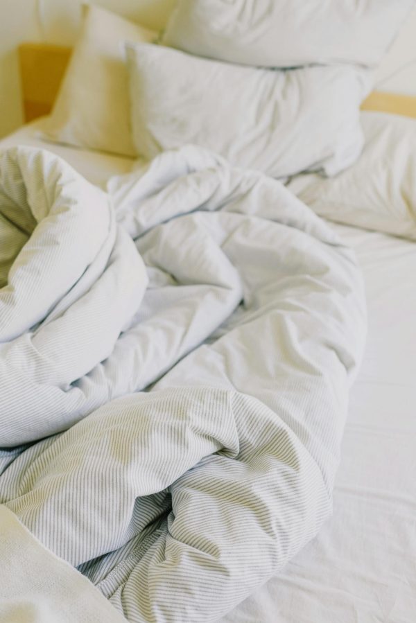 From above of comfortable messy with soft white blanket and pillows in sunny morning