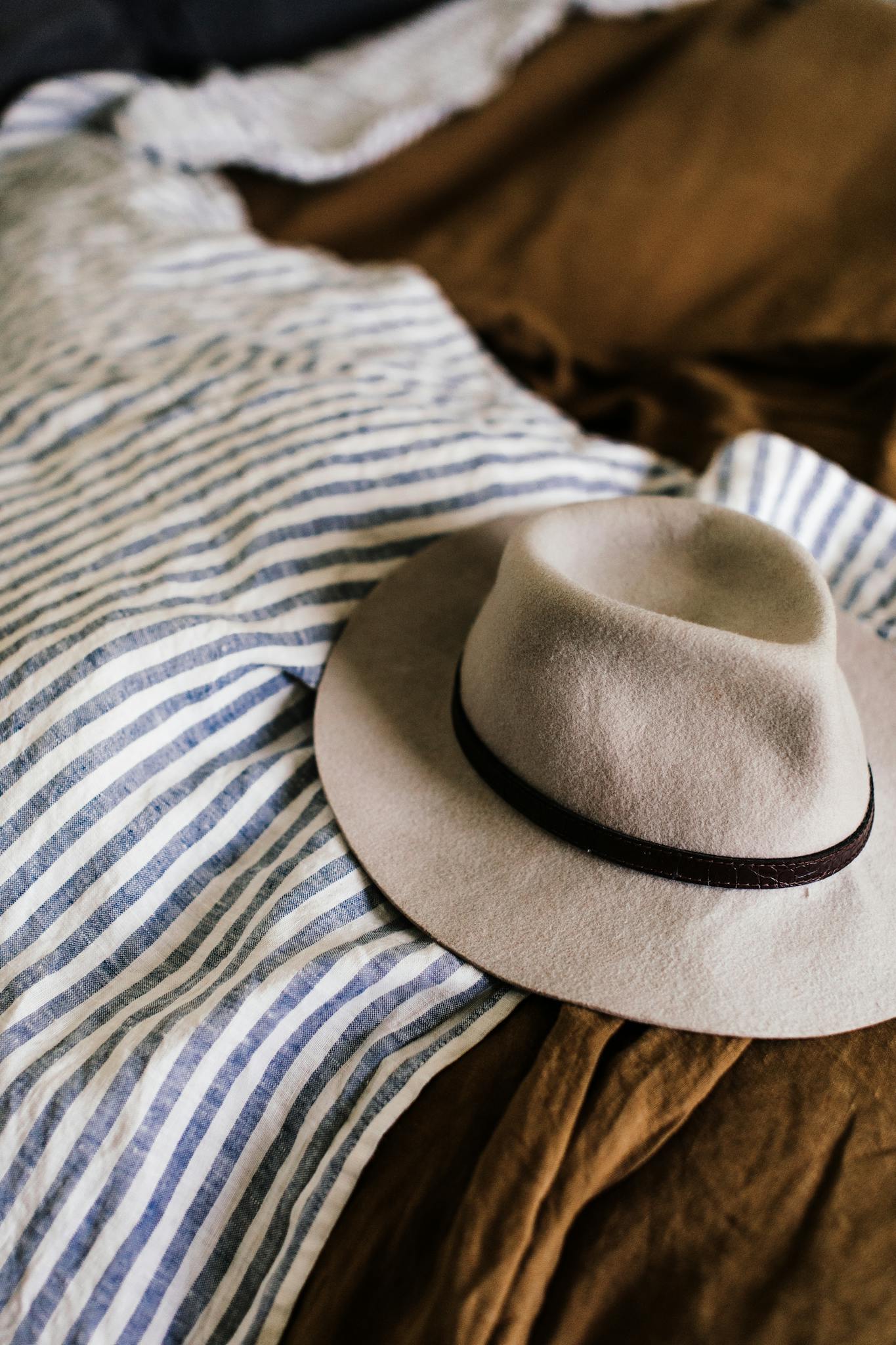 From above of hat placed on unmade bed with duvet with stripes in bedroom